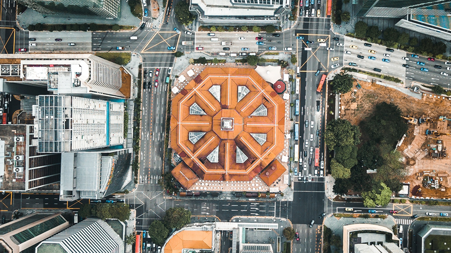Aerial view of a dense urban intersection with a distinctive octagonal building featuring an orange roof at the center, surrounded by high-rise offices, streets, and traffic, illustrating modern city infrastructure and capital markets activity.