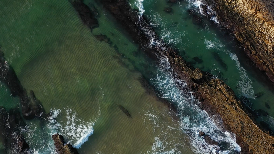 Aerial view of a rocky coastline with turquoise water, gentle waves, and patterned sand formations. The natural shoreline landscape introduces Apollo’s 2025 Responsible & Sustainable Portfolio Supplement and its sustainability reporting highlights.