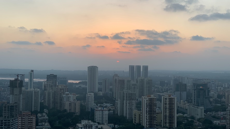 Cityscape at sunset with high-rise buildings and a partially cloudy sky; the sun near the horizon casts an orange glow—symbolizing Apollo’s regional presence in India.