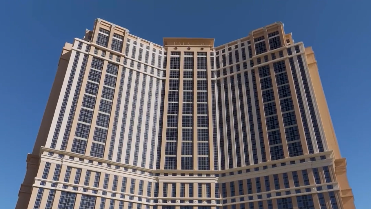 Wide-angle view of The Venetian Resort in Las Vegas showing its tall, symmetrical tower with grid-patterned windows and beige accents under a clear blue sky.