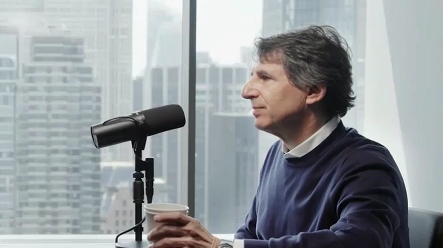 Speaker seated in a recording studio speaks into a podcast microphone with a city skyline visible through large windows. Side-profile portrait illustrating a discussion on private credit and alternative investments.
