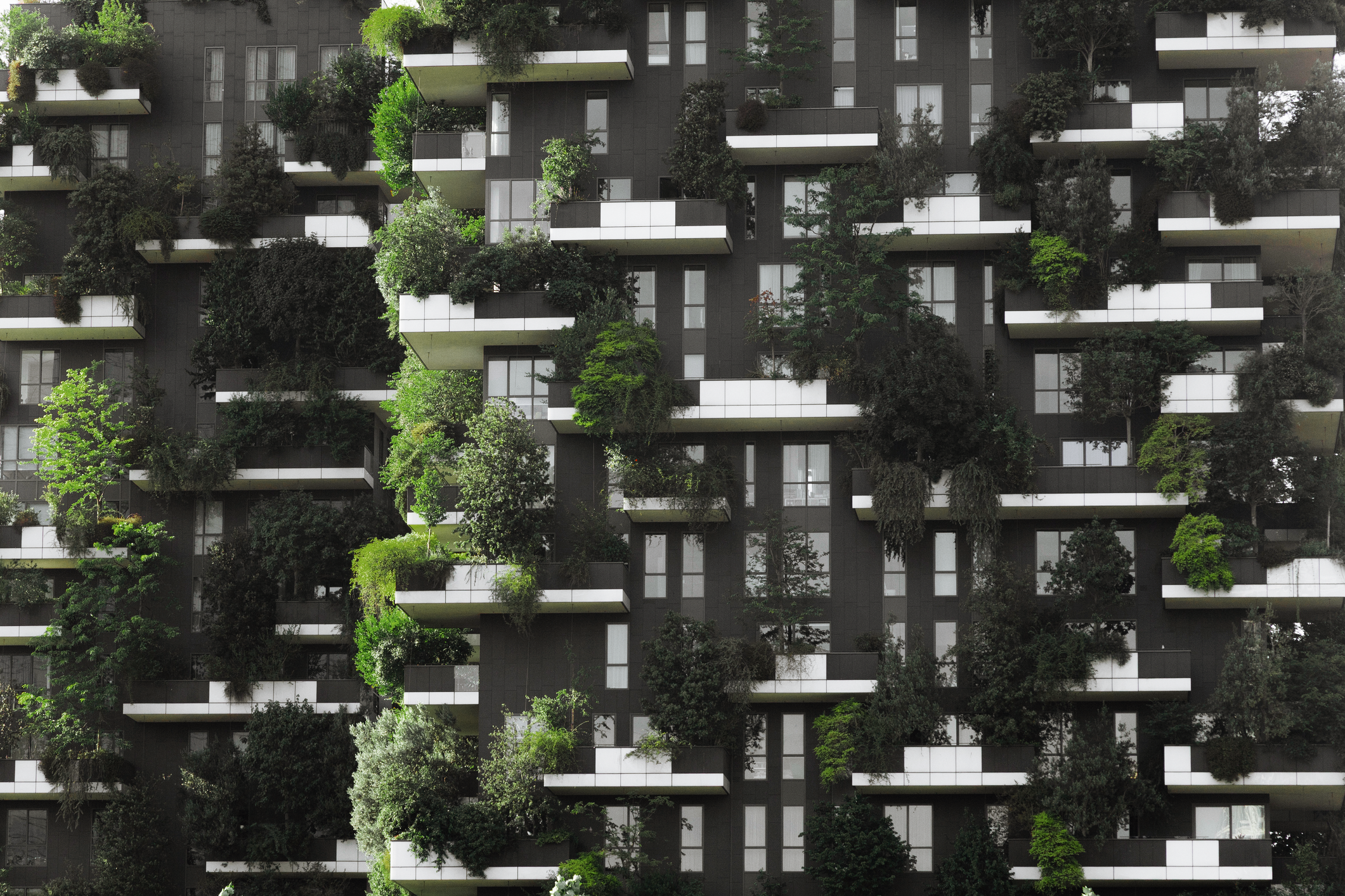 Modern residential building with layered balconies covered in dense greenery and trees, illustrating sustainable urban design and real assets in private markets, aligned with themes of private credit and long-term asset allocation