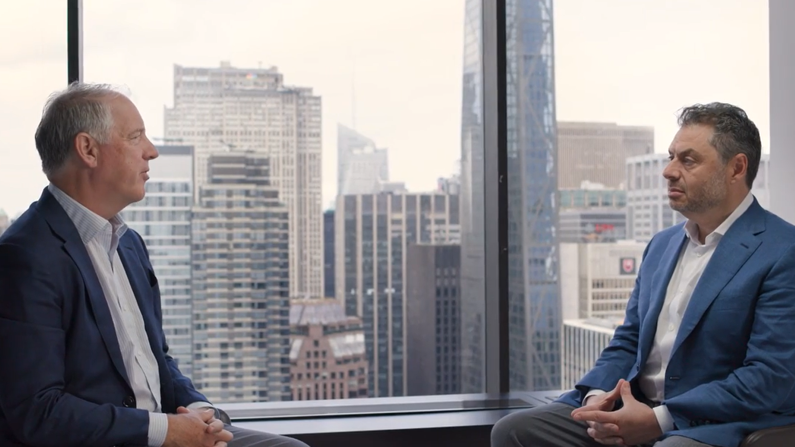 Jim Zelter and Eric Needleman sit across from each other in a modern office overlooking a city skyline, engaged in a discussion on private credit, capital solutions, and evolving strategies within asset management and private markets.