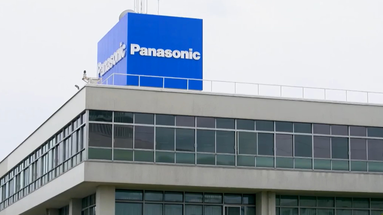 Modern commercial building with glass windows and a large blue Panasonic sign mounted on the rooftop, representing Panasonic Holdings and its automotive systems division