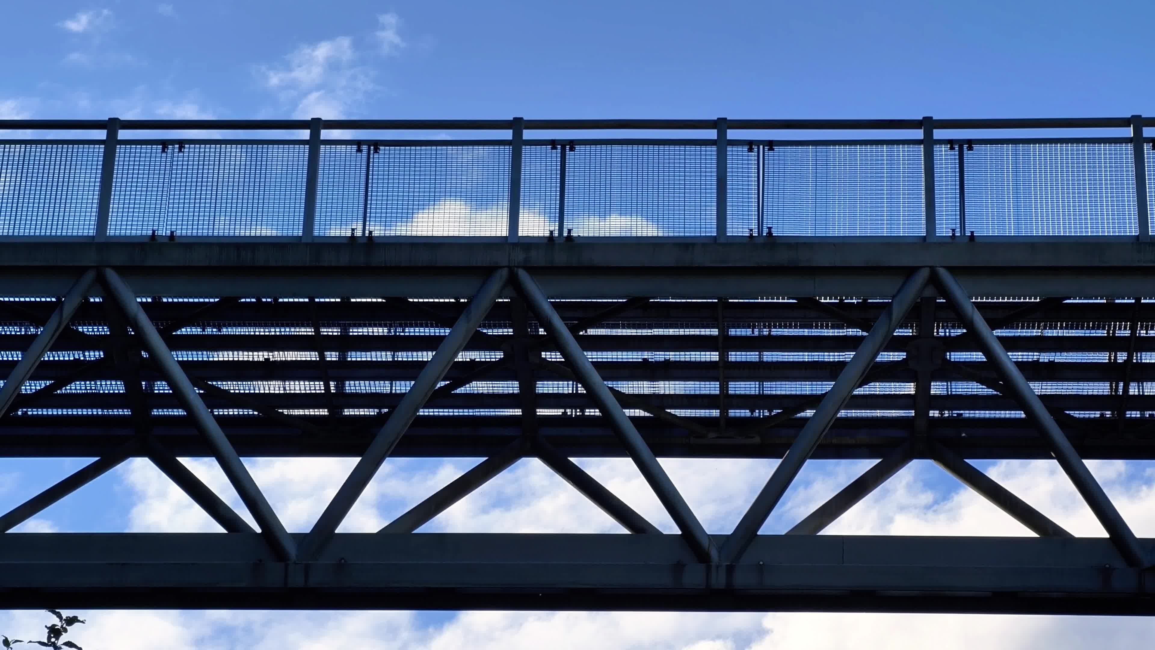 Steel bridge or elevated walkway structure viewed from below against a blue sky with clouds, featuring intersecting beams and railings, symbolizing connectivity within private markets and investment frameworks.