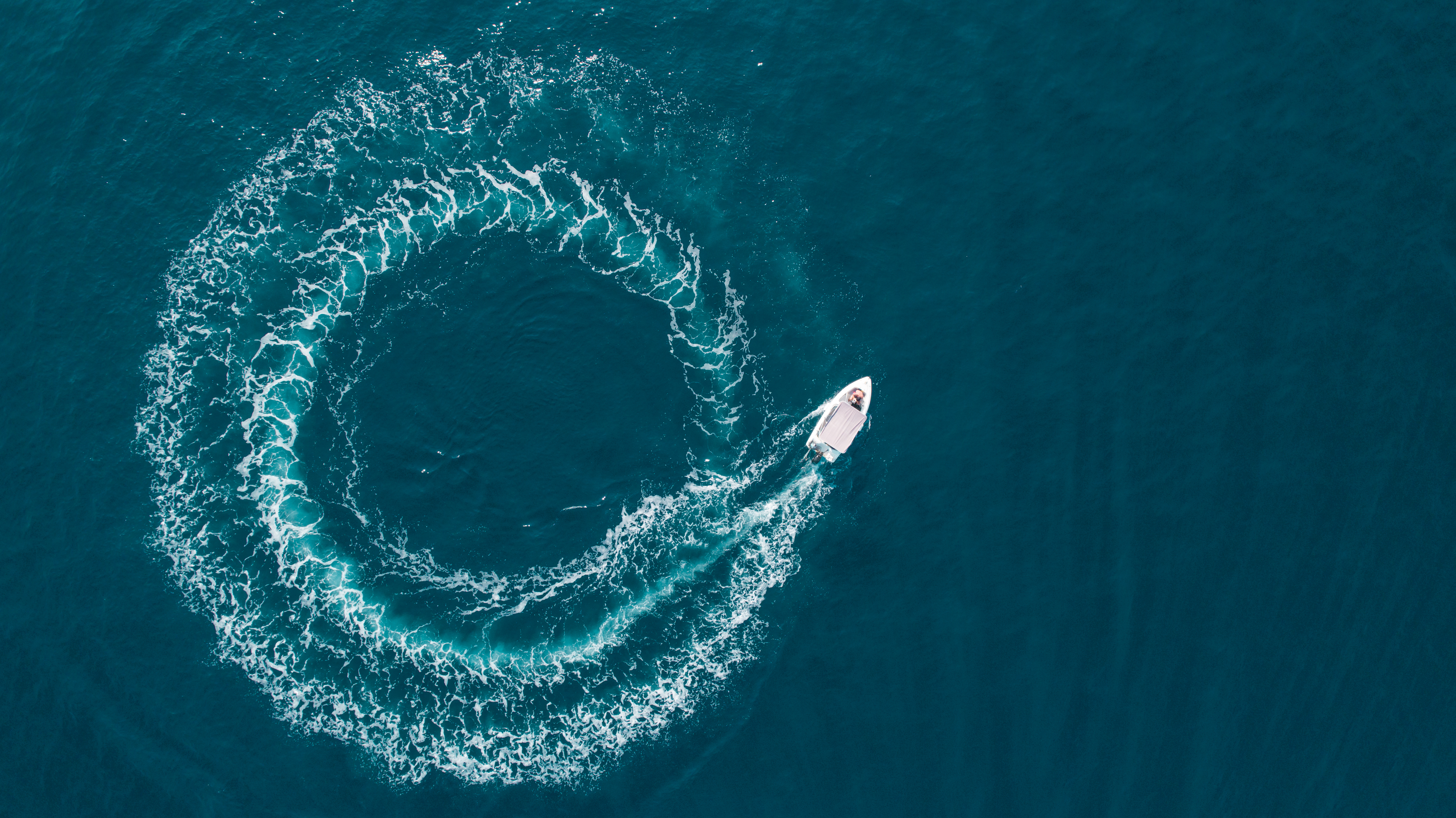 Aerial view of a small motorboat carving a circular wake across deep blue ocean water, creating a striking ring pattern that symbolizes a fresh perspective on portfolio construction and private credit in the context of private investment grade credit.