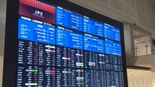 Large electronic display board inside a stock exchange showing JPX market data, including stock prices, indices, and trading volumes, reflecting real-time activity in public equity and capital markets trading.