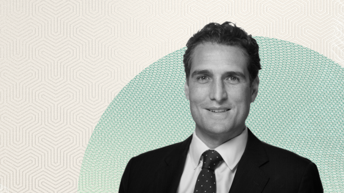 Black-and-white portrait of John Cortese in a dark suit and polka-dot tie, smiling in front of a beige and green textured background.