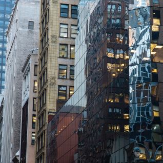 Street-level view of modern glass and historic stone office buildings along Madison Avenue in New York City, highlighting reflective façades, dense urban architecture, and the commercial business district.