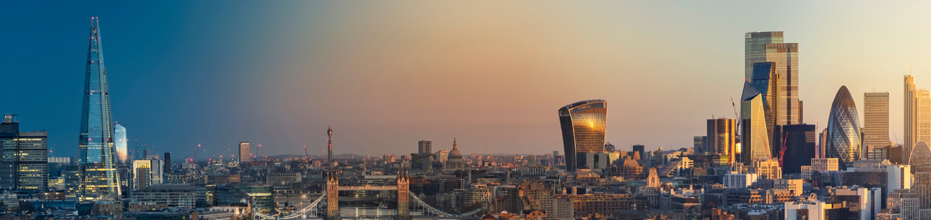 Panoramic view of London's skyline at sunset, featuring The Shard, Tower Bridge, St. Paul's Cathedral, the Walkie Talkie building, and the Gherkin, with modern skyscrapers across the financial district.