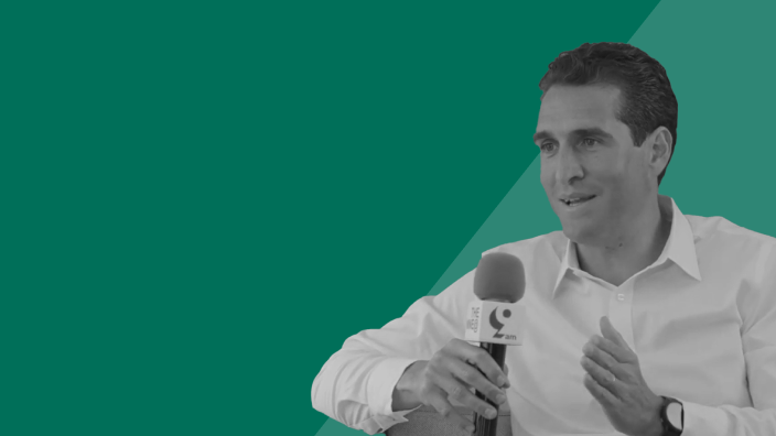 John Cortese, Apollo Partner and Head of Portfolio Management, speaks into a handheld microphone during an interview, discussing private credit markets, origination, and investment opportunities against a green studio background.