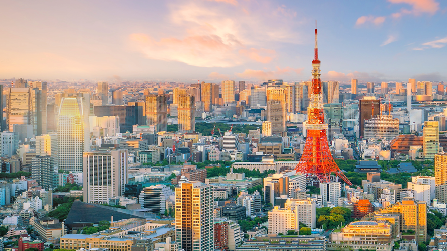 Panoramic view of Tokyo’s skyline at sunset with Tokyo Tower illuminated in orange-red, surrounded by high-rise office buildings and residential districts, illustrating the scale of Japan’s urban capital markets and financial center.